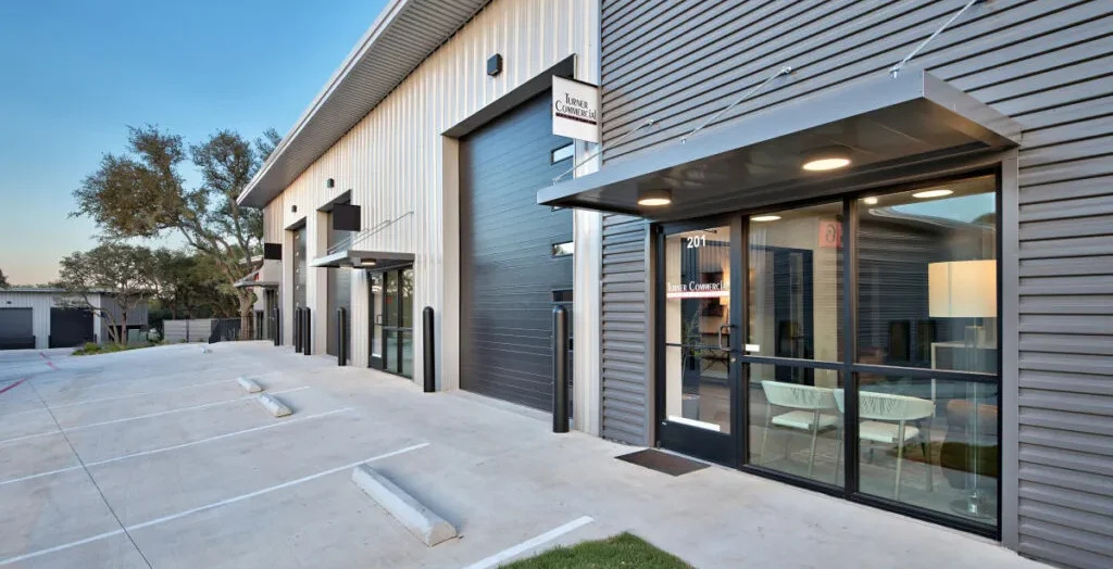 Modern hybrid office and warehouse flex space in Central Texas featuring large glass windows, roll-up garage doors, and dedicated parking spots.