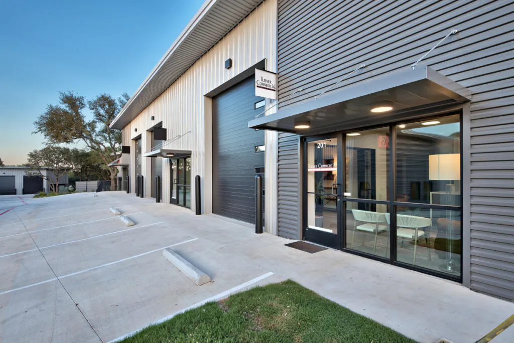 Modern hybrid office and warehouse flex space in Central Texas featuring large glass windows, roll-up garage doors, and dedicated parking spots.